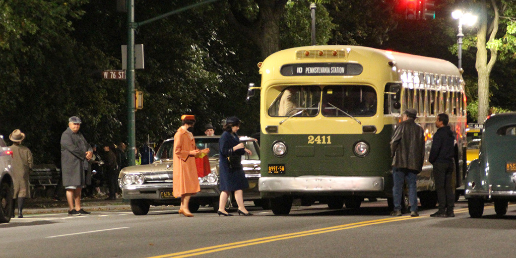 Background players loading onto a bus during rehearsal