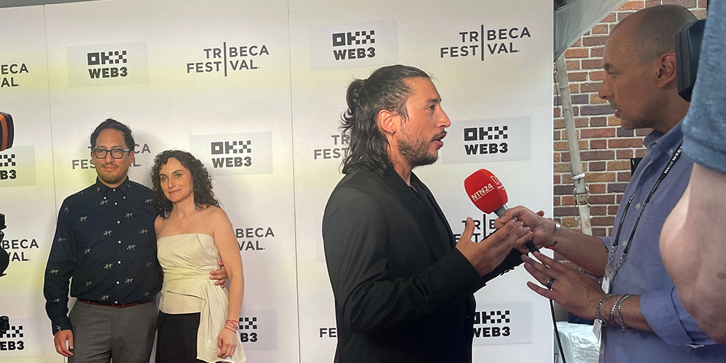 Alvaro Manzano Zambrana and Gabriela Maire posing, and Director Vinko Tomicic foreground being interviewed by Nuestra Tele Noticias